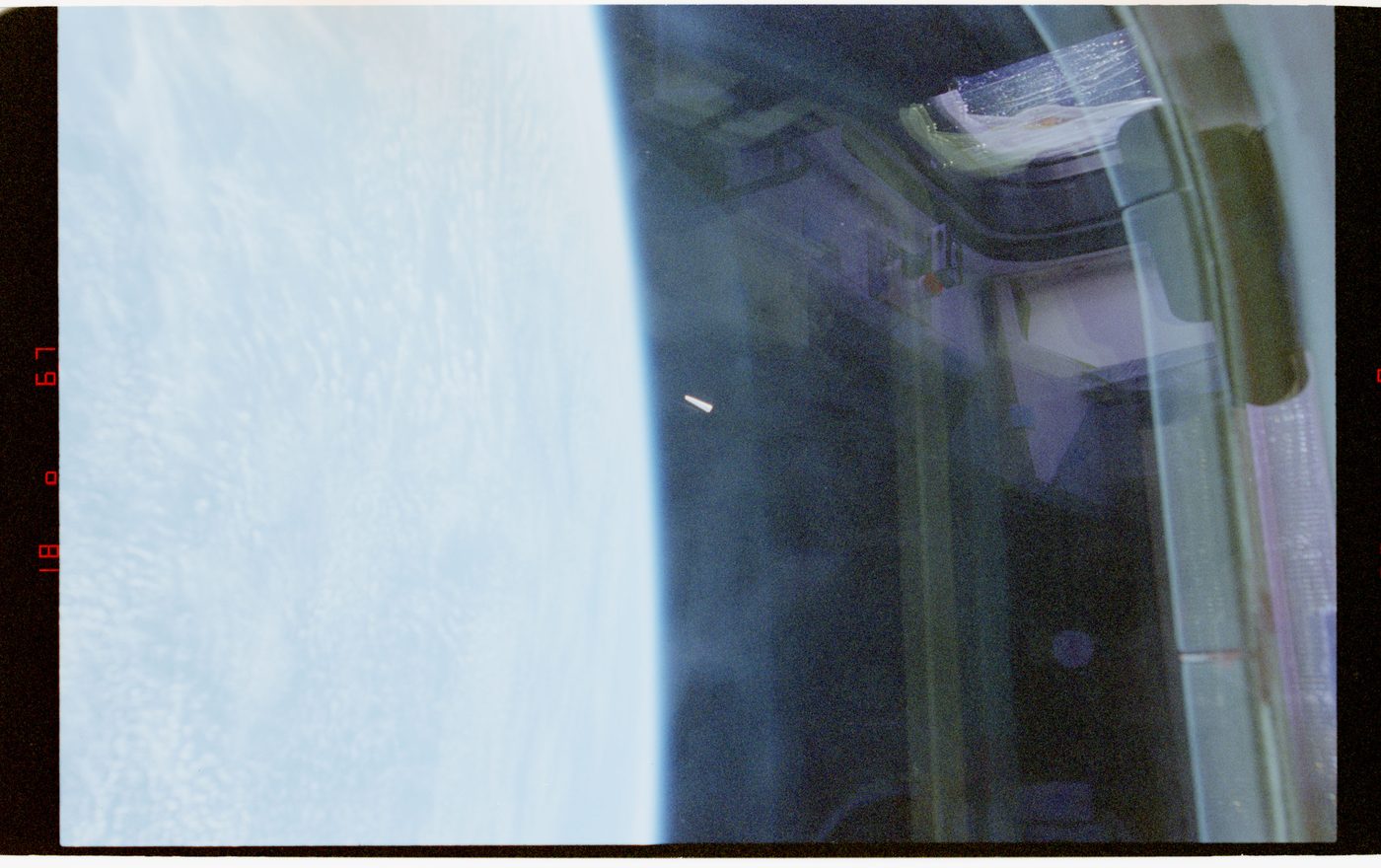 NASA photograph from STS-80 showing a small white object in low Earth orbit near the limb of the Earth, seen through the shuttle window